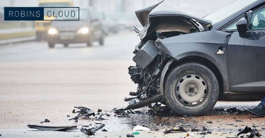 Car crash with the car in the forefront having severe front-end damage