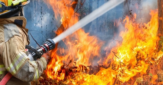 Firefighter with a hose spraying water at a large fire